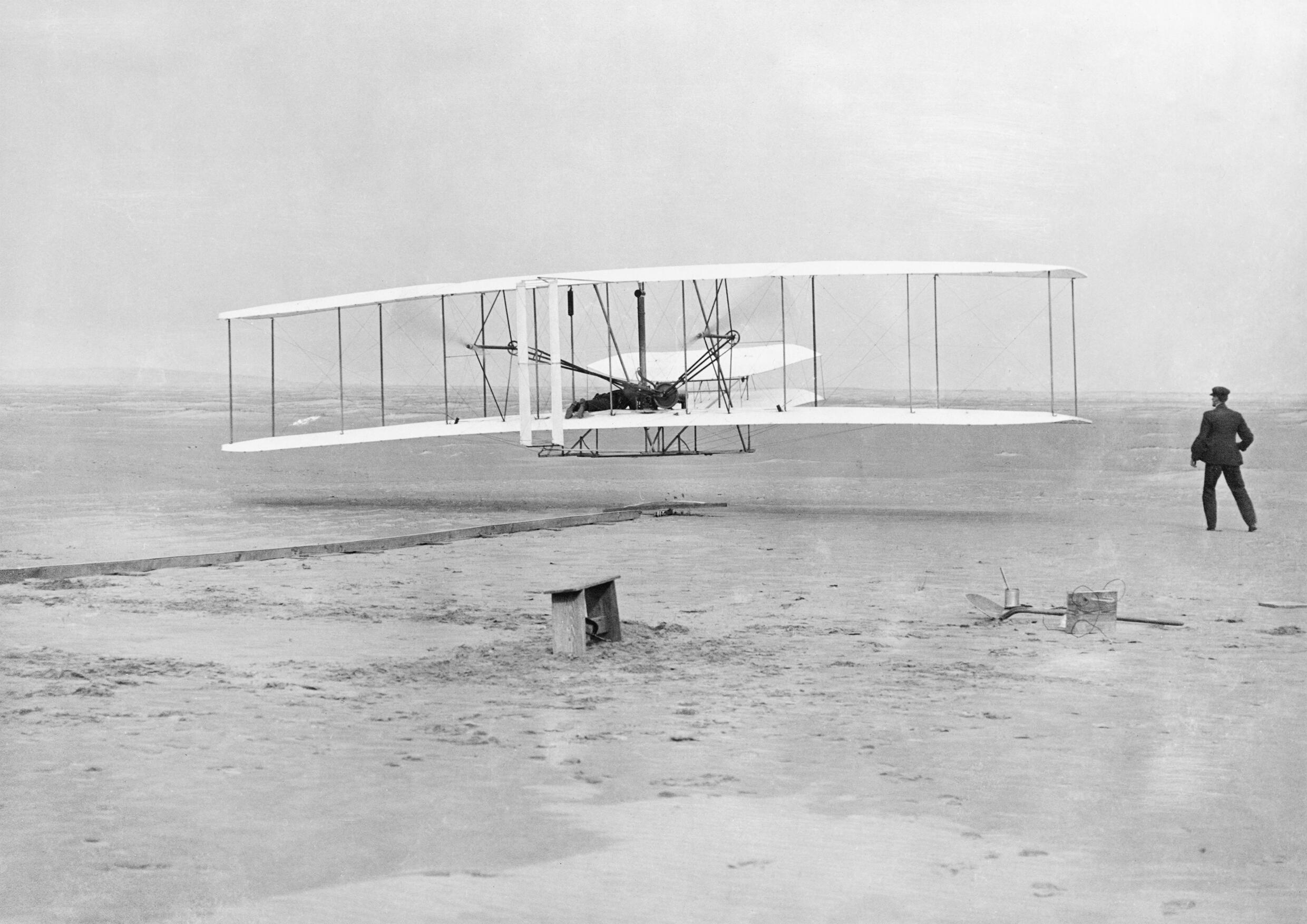 The Wright Flyer airborne during the first powered flight at Kitty Hawk, North Carolina, December 17, 1903, with Orville Wright at the controls and Wilbur running alongside
