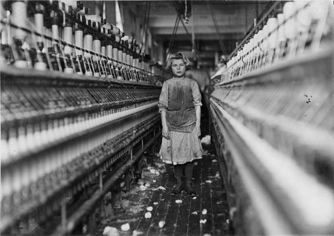 Workers, including children, on an industrial factory floor beside unguarded belt-driven machinery, the kind of workplace whose accidents gave rise to workers' compensation insurance