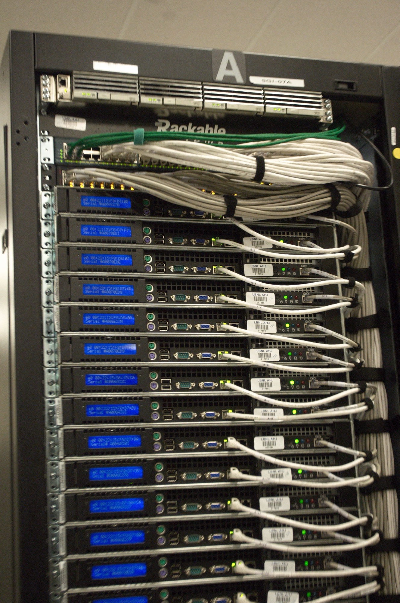Close up of the rear of a server rack at a national laboratory data center, rows of blue status LEDs and bundled ethernet cables.