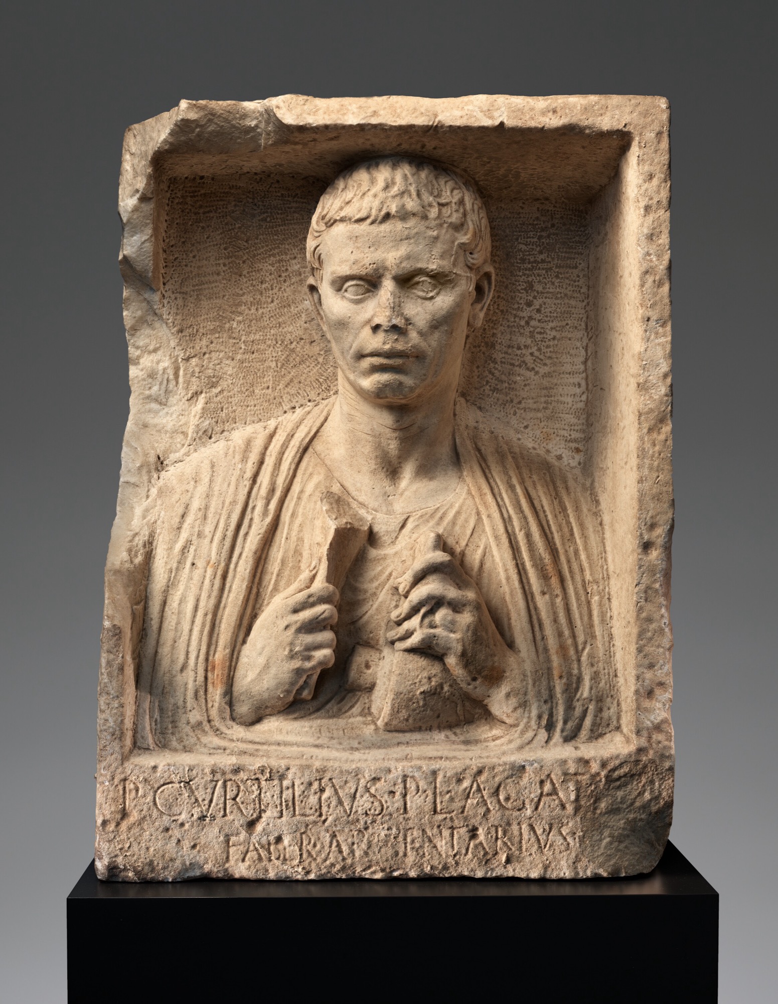 Marble funerary relief of a Roman freedman silversmith holding his tools, with a Latin inscription naming his trade below.